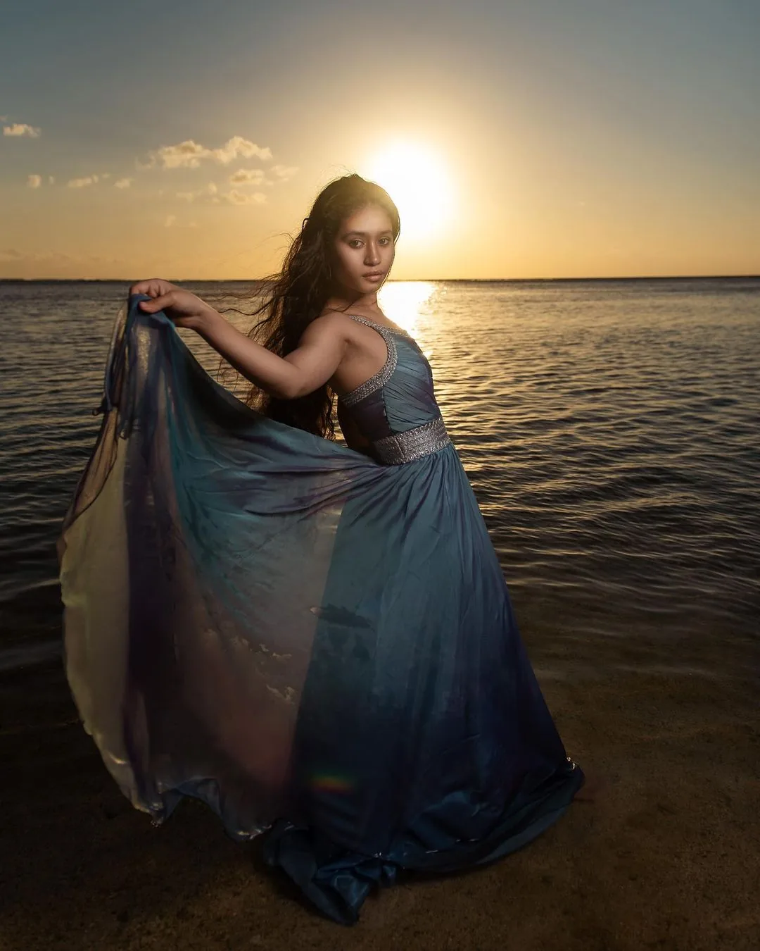 Woman posing in a long blue dress along the Mauritius coastline during sunset